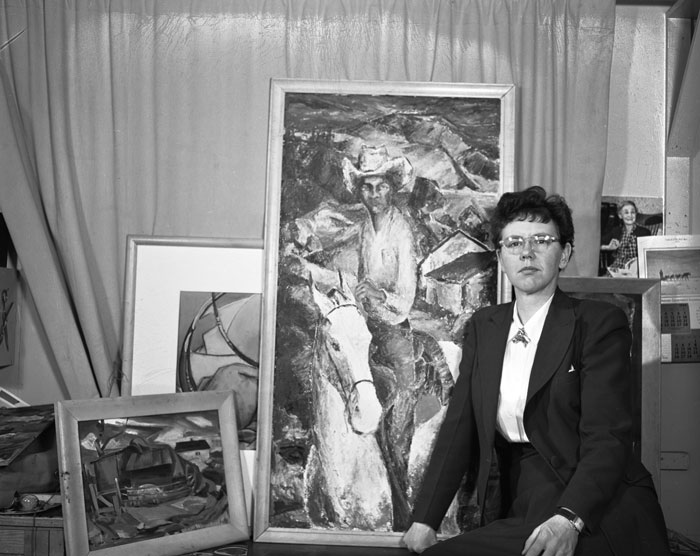 Black and white image of Wynona Mulcaster in front of a selection of her paintings in 1950